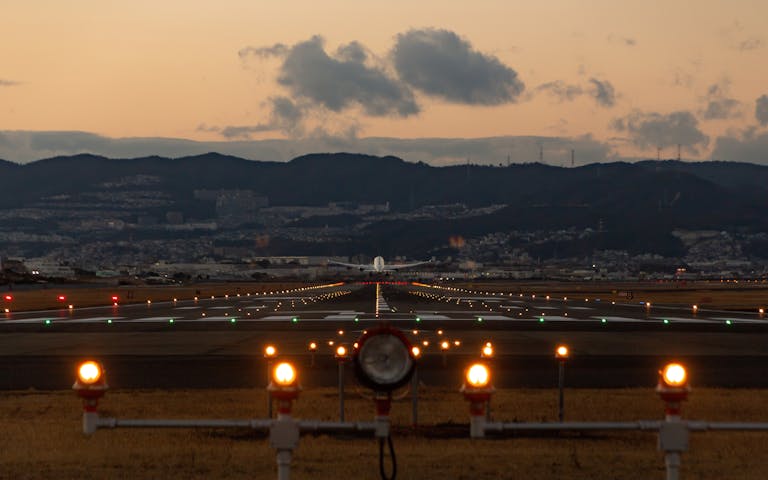 Scenic view of airplane landing on Osaka runway during dusk with city skyline.